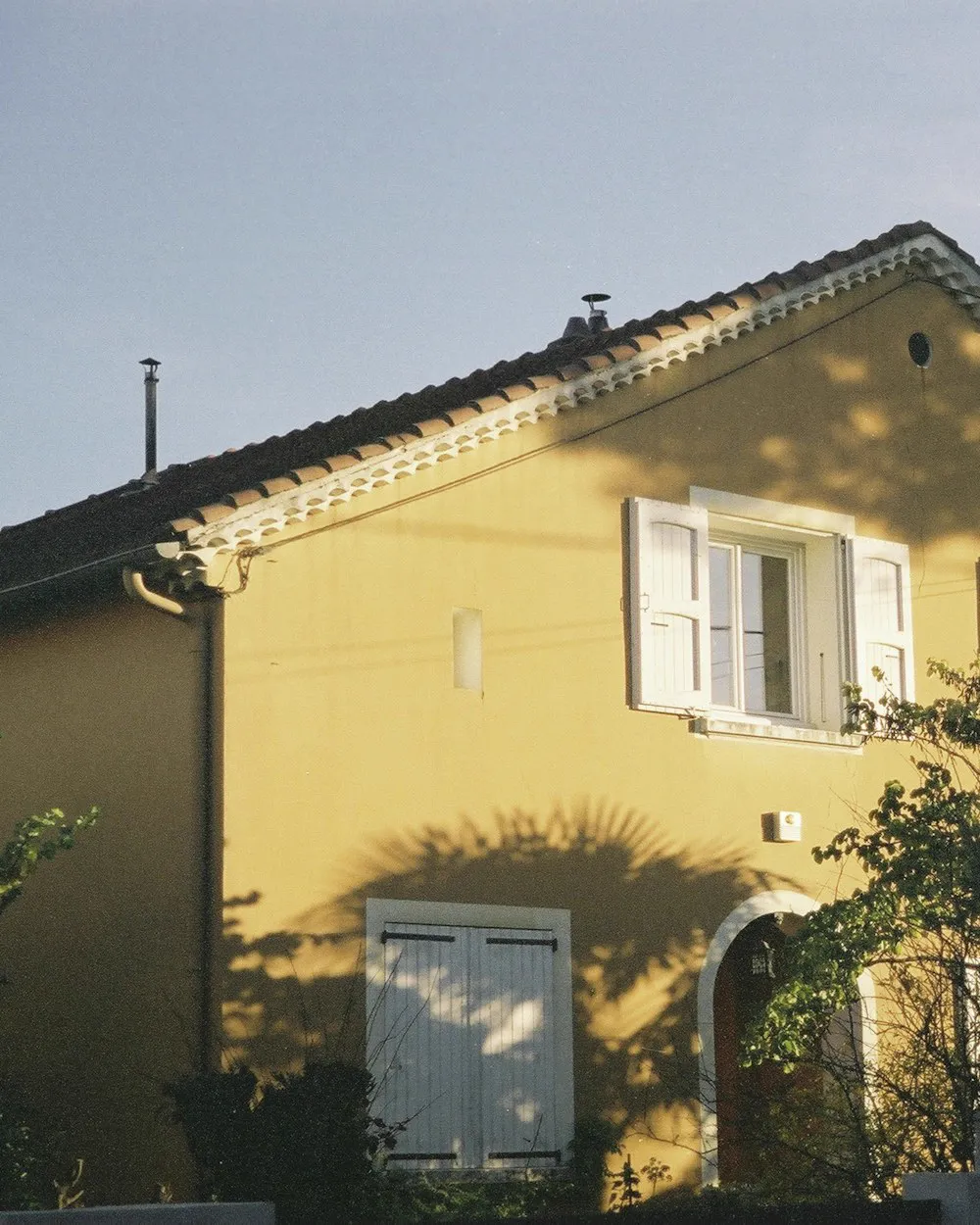 Un pavillon aux murs jaunes et volets blancs, derrière un jardin