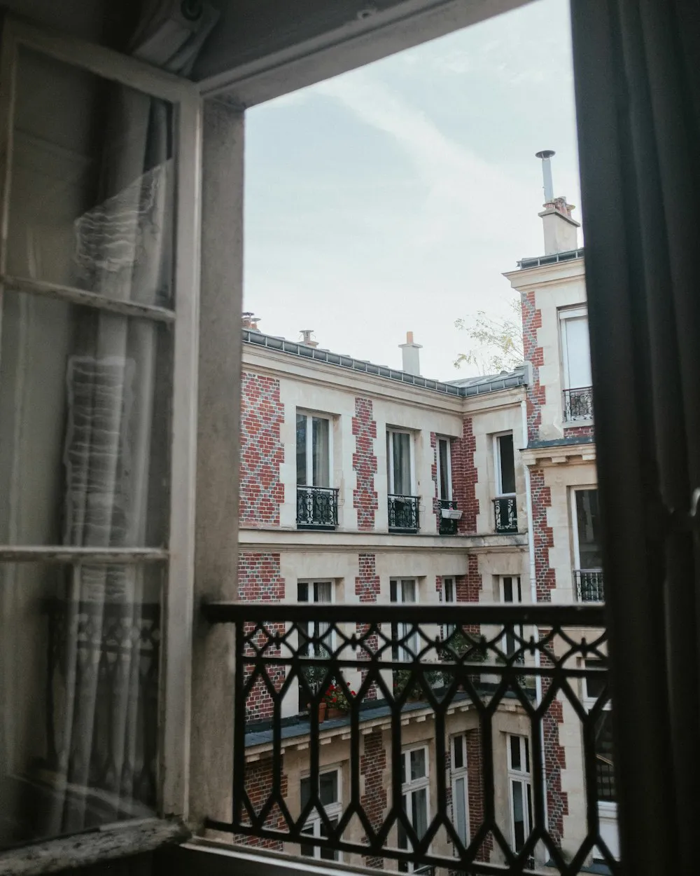 Une fenêtre ouverte sur les immeubles parisiens, derrière un garde-corps en fer forgé